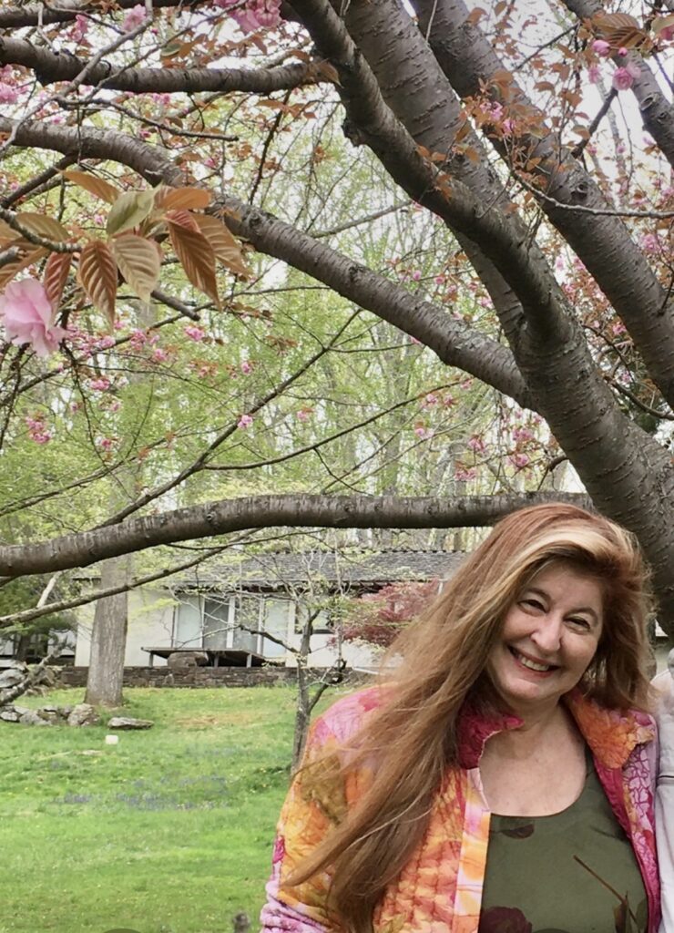 Miriam smiling woman standing near a tree showing a bough of cherry blossoms