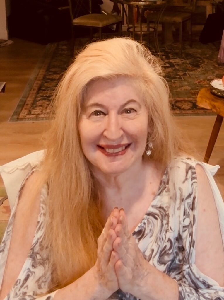 Smiling woman Miriam Belov with hands in prayer posture.
